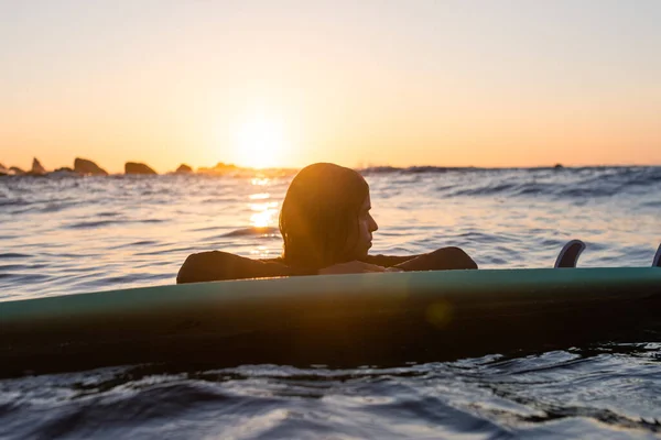 Szörfös lány várja a hullámot a vízben naplementekor — Stock Fotó
