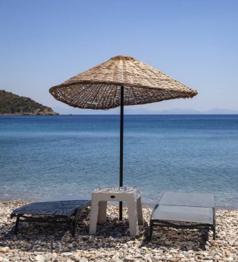 Wicker Sunshade şemsiyesi ve sahilde iki boş güneş panzesi. Tatil konsepti. Peyzaj