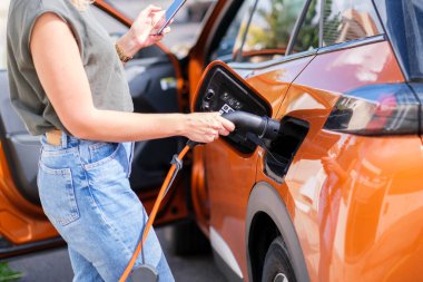 Kadın elleri elektrikli araba şarj aletini bağlıyor.