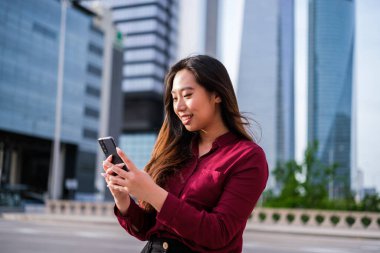 Finans bölgesinde akıllı telefon kullanan genç bir iş kadını.