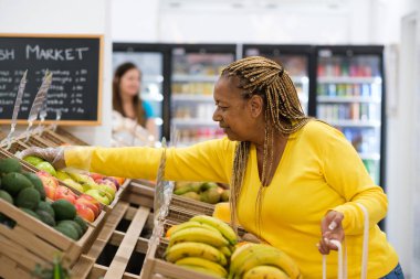 Orta yaşlı bir kadın marketten meyve ve sebze alıyor.
