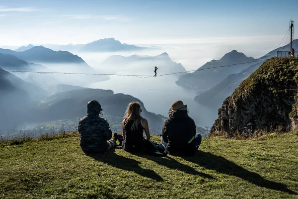 brave woman on slackline in mountains over lake with spectators in the foreground