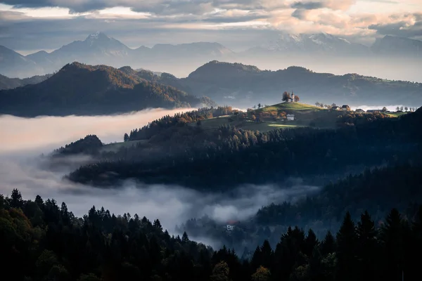 alpine landscape with church in mountains and fog in the morning