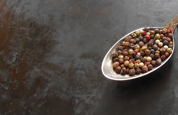 Gri metalik zemin üzerinde gümüş bir kaşık üzerinde renkli biber tanecikleri ve metin için boşluk