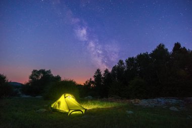 Alacakaranlıkta gökyüzünde Samanyolu ile aydınlatılmış sarı çadır
