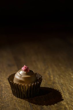 Single spot lighted rasberry toped chocolate praline on a wooden shelf