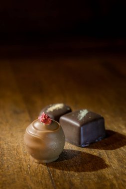 Group of different spot lighted chocolate praline on a wooden shelf