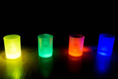 Four shot glasses illuminated in different colors green, yellow, blue and red