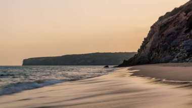 Orange evening sky at beach with silhouette of rocks in background at praia da Figueira, Portugal
