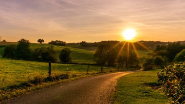 rural landscape with country road and green meadows at sunset, Roehn Mountains, Germany