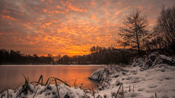 Spectacular sky at dawn with frozen lake and winter landscape