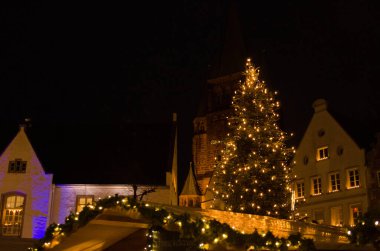 Warendorf 'taki Alman noel pazarında aydınlatılmış Noel ağacı. Arka planda kilise var.