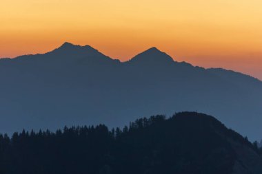 Slovenya, alacakaranlıkta ağaçlı dağların siluetleriyle atmosferik alp manzarası