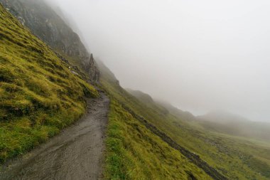 İskoçya 'nın Skye adasında sisli bir sabahta, yeşil dağlarda bomboş bir patika.