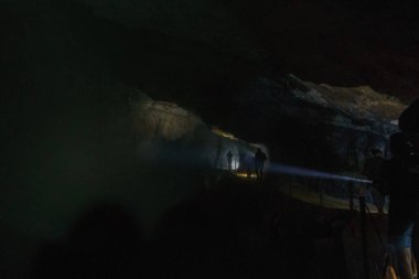 Karanlık mağarada el fenerleriyle yürüyen insanlar