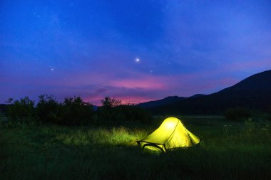 Alacakaranlıkta sarı yeşil kamp çadırı yıldızlarla aydınlandı.