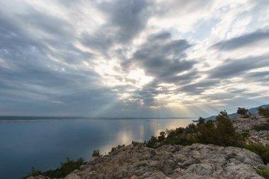 Güneş ışınları Hırvat denizinin üzerinden bulutların arasından geçiyor