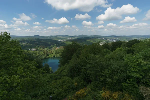 Gemuenden Maar, çevresi ormanlarla çevrili tepe manzaralı ve arka planda Daun şehri, Almanya, Daun