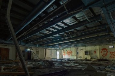 Eski bir sanayi üssünde, tavanında kırık elektrik düğmeleri ve boruları olan bir yerde.