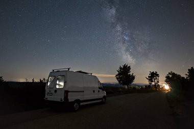 Milky Way over illuminated camper van and silhouette of trees, Black Forest, Germany