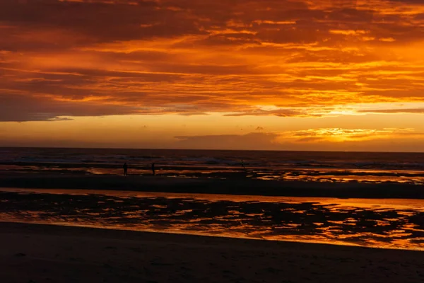 Kuzey Denizi 'nin üzerinde karamsar bulutlu gökyüzü ve Belçika' nın De Haan şehrinde yaşayan insanların silueti ile güzel bir gün batımı..