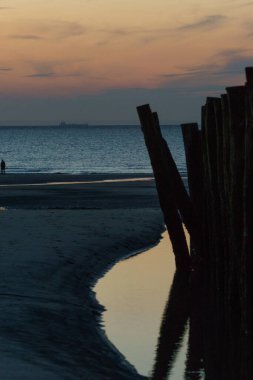 Fransa 'nın Opal Sahili, Wissant sahilinde akşam alacakaranlığında sakin su yüzeyine yansıyan ahşap dalga kırıcı.