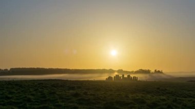 Stonehenge ve koyunların İngiltere ve İngiltere 'de dolaştığı kırsal alanda karamsar, sisli bir gün doğumu.
