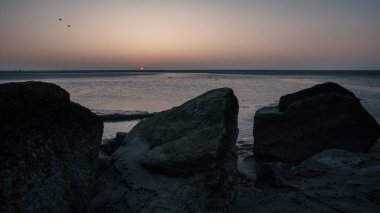 Atlantik kıyısında kasvetli, karanlık ve puslu bir gün batımı Mont Saint Michel, Normandiya, Fransa yakınlarındaki kayalıklarla