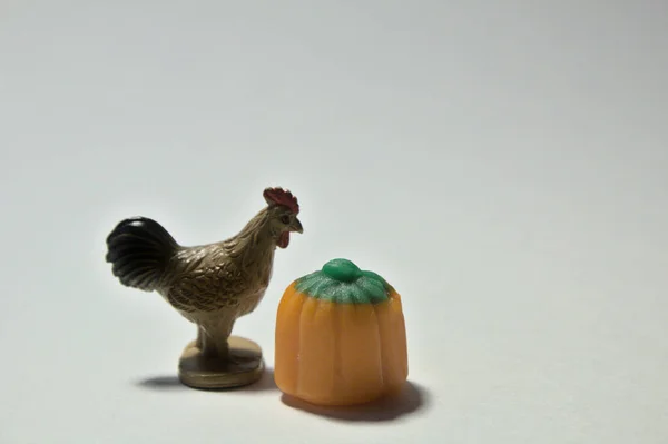 Close up of a toy chicken next to a candy pumpkin on a white background.