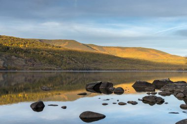 Gün batımı, kayalarla dolu bir buzul gölüne yansıyor. Sanabria Gölü, İspanya. 