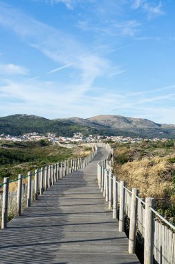 Doğayla çevrili ahşap geçit ve arka planda küçük bir kasaba. Bulutlu mavi gökyüzü. Yüksek kalite fotoğraf