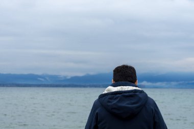 Mans back looking at Lake di Garda, Italy, with mountains in the background