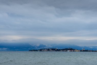 View of Lake di Garda, Italy, with mountains filled with snow and clouds on the background. 