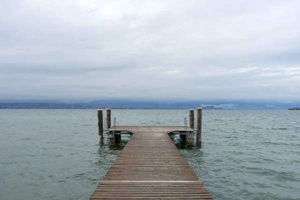 Pier on the Lake di Garda, italy, with snow capped mountains and clouds in the background. High quality photo