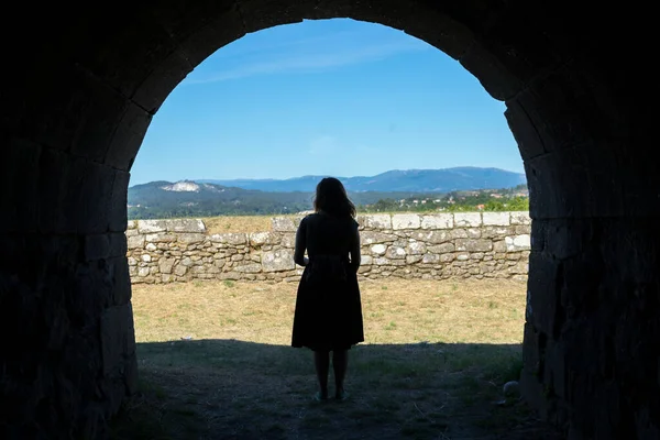 Womam silhouette on a ancient stone tunnel looking from behind with mountains in background