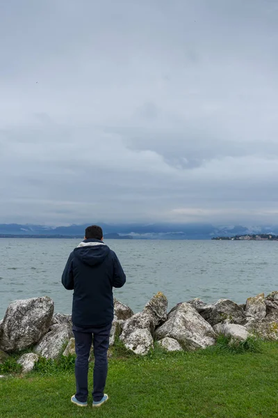 Mans back looking at Lake di Garda, Italy, with mountains in the background