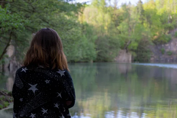 Woman looking at a lake in the Czech Republic with trees in the background.