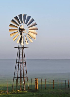 Yel değirmeni su pompası ve gün doğumunda şehir yolu olan bir manzara.
