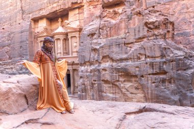 Geleneksel kıyafetler ve başörtüsü takmış arka plandaki kayanın tepesinde kalan kadın Petra Sarayı.