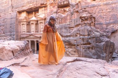 Geleneksel kıyafetler ve başörtüsü takmış arka plandaki kayanın tepesinde kalan kadın Petra Sarayı.