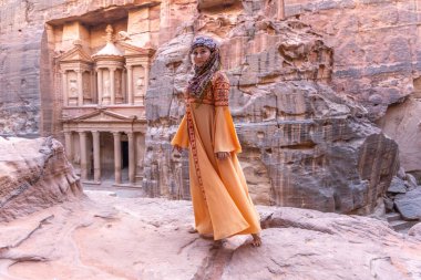 Geleneksel kıyafetler ve başörtüsü takmış arka plandaki kayanın tepesinde kalan kadın Petra Sarayı.
