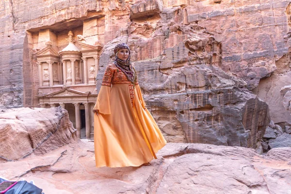 Geleneksel kıyafetler ve başörtüsü takmış arka plandaki kayanın tepesinde kalan kadın Petra Sarayı.