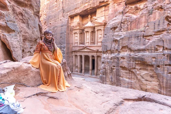 Geleneksel kıyafetler ve başörtüsü takmış arka plandaki kayanın tepesinde kalan kadın Petra Sarayı.