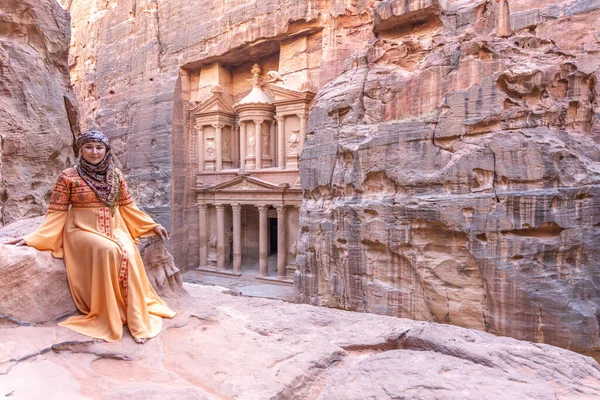 Geleneksel kıyafetler ve başörtüsü takmış arka plandaki kayanın tepesinde kalan kadın Petra Sarayı.