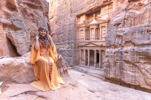Geleneksel kıyafetler ve başörtüsü takmış arka plandaki kayanın tepesinde kalan kadın Petra Sarayı.