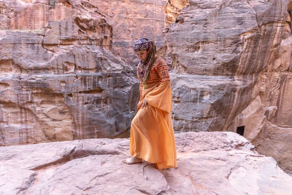 Geleneksel kıyafetler ve başörtüsü takmış arka plandaki kayanın tepesinde kalan kadın Petra Sarayı.