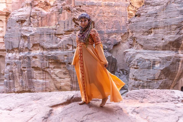 Geleneksel kıyafetler ve başörtüsü takmış arka plandaki kayanın tepesinde kalan kadın Petra Sarayı.