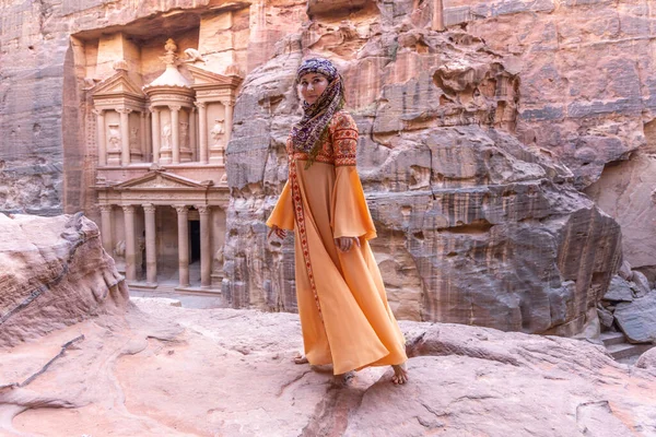 Geleneksel kıyafetler ve başörtüsü takmış arka plandaki kayanın tepesinde kalan kadın Petra Sarayı.