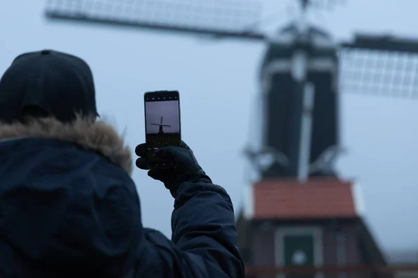 Sabahın köründe telefonuyla yel değirmeninin fotoğrafını çeken adam.