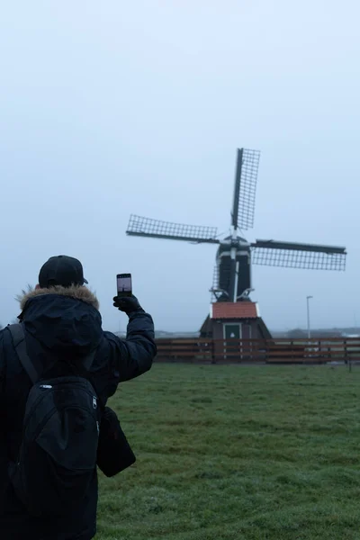 Sabahın köründe telefonuyla yel değirmeninin fotoğrafını çeken adam.